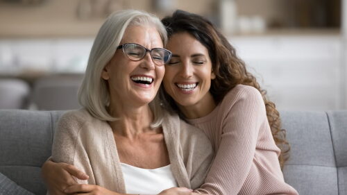Mulher mais velha e mulher mais jovem se abraçando no sofá.