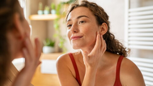 woman looking in mirror adult acne care findings from Kenvue.jpeg